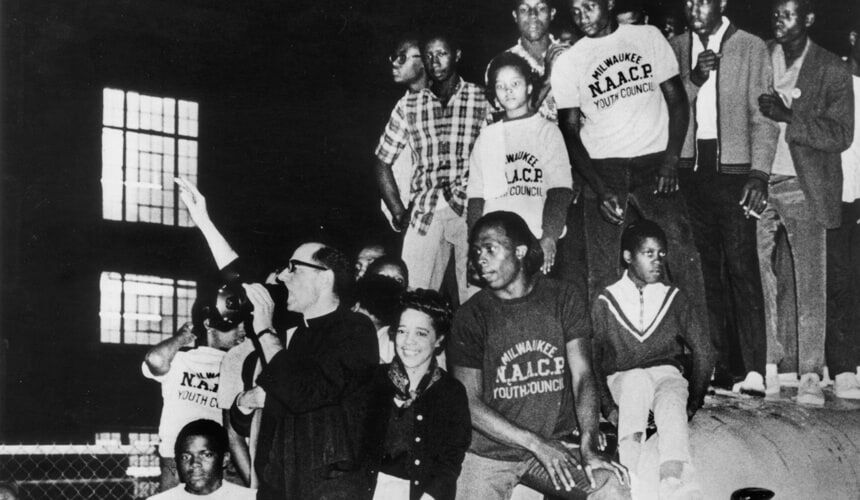 Father Groppi and Vel Phillips on the hood of bus at a protest. (Image courtesy of the Wisconsin Historical Society, #48149.) Father Groppi and Vel Phillips on the hood of bus at a protest.