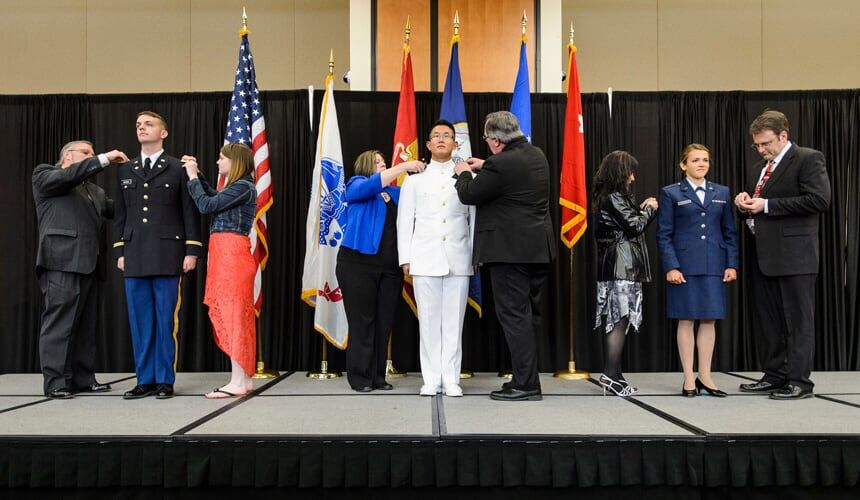 Family members help with a pinning ceremony as graduates from UW-Madison's Army, Navy and Air Force ROTC units participate in the 2016 officer commissioning ceremony. (Image courtesy of University Communications, #22518. Photo by Jeff Miller.) Graduates from UW-Madison's Army, Navy and Air Force ROTC units being pinned by theier family members during the officer commissioning ceremony.