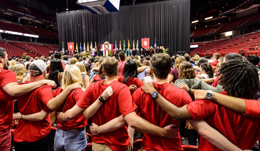 First-year students link arms and sing "Varsity" at the end of the Chancellor's Convocation for New Students, a Wisconsin Welcome event held at the Kohl Center.